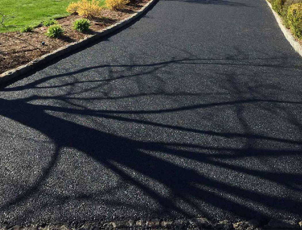00001residential-1050x800-1 A newly-paved asphalt path with the shadow of a leafless tree cast across it. Green grass and mulch beds line the edges of the path on a sunny day.