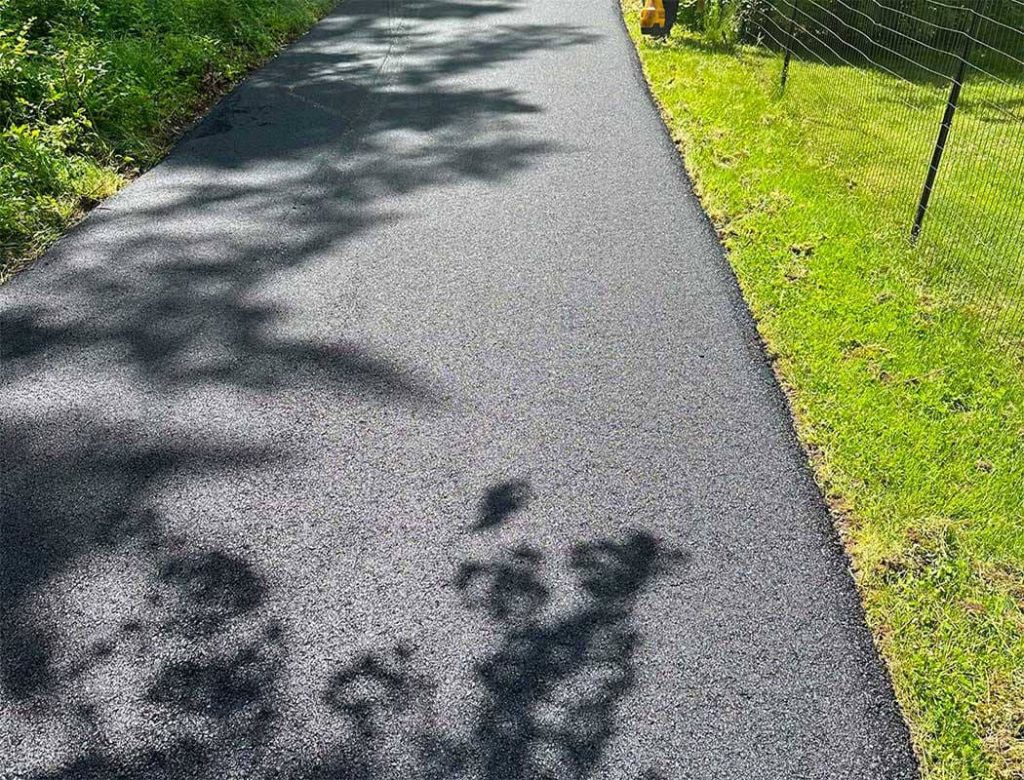 Freshly paved asphalt path with shadows from trees and grass on either side.
