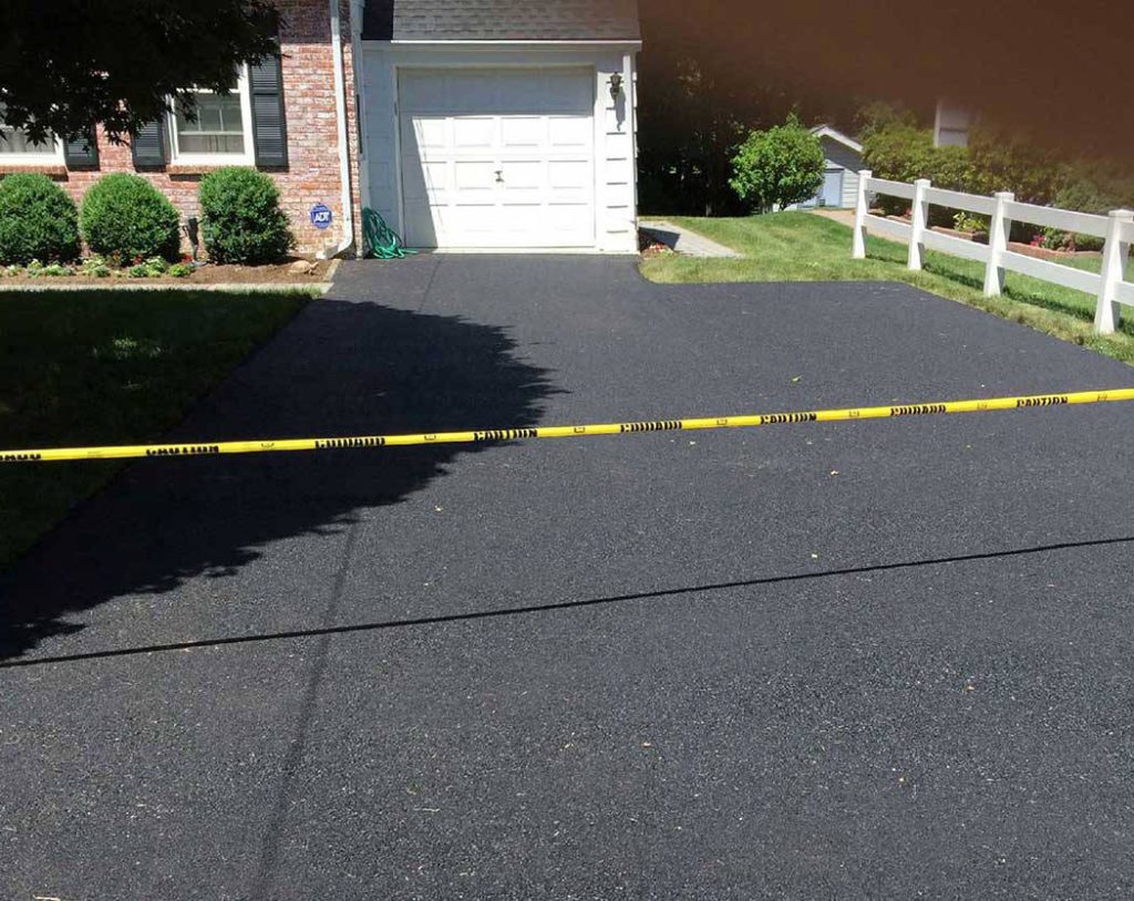 Driveway with fresh asphalt is blocked by yellow caution tape in front of a house and garage.