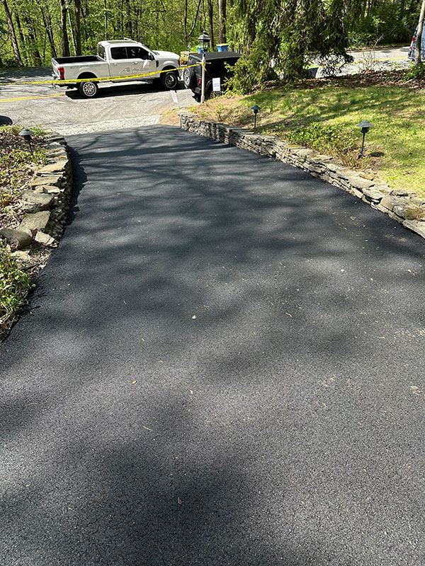 Freshly paved black asphalt driveway with stone borders, leading to a parked white pickup truck.