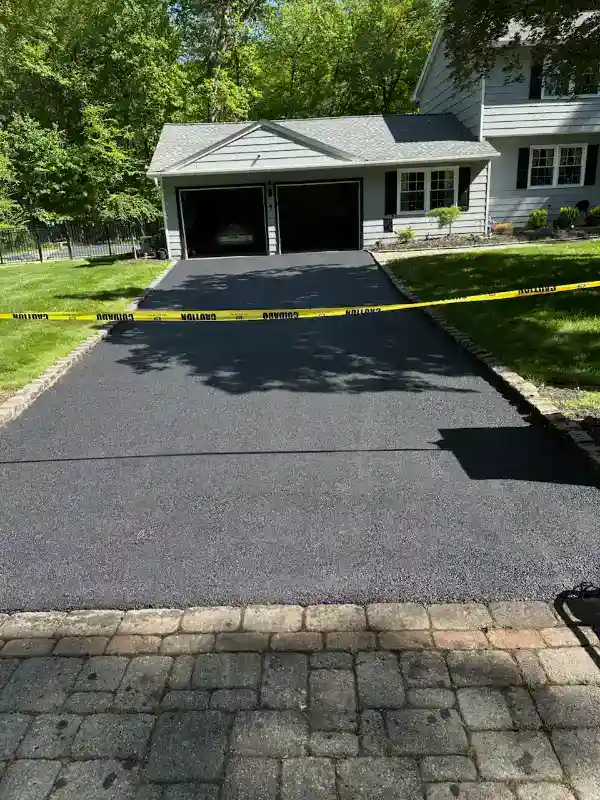 Freshly paved driveway blocked by caution tape in front of a house with a two-car garage.
