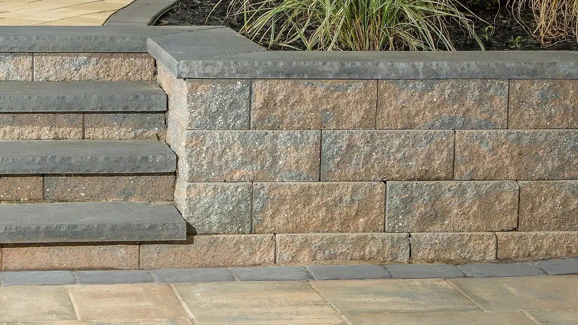 Stone stairs and a low retaining wall with plants behind, next to a paved patio area.
