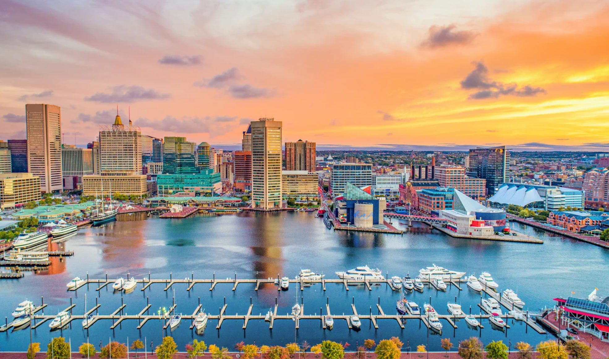 MD-img Baltimore harbor skyline at sunset with boats docked and colorful clouds in the sky.